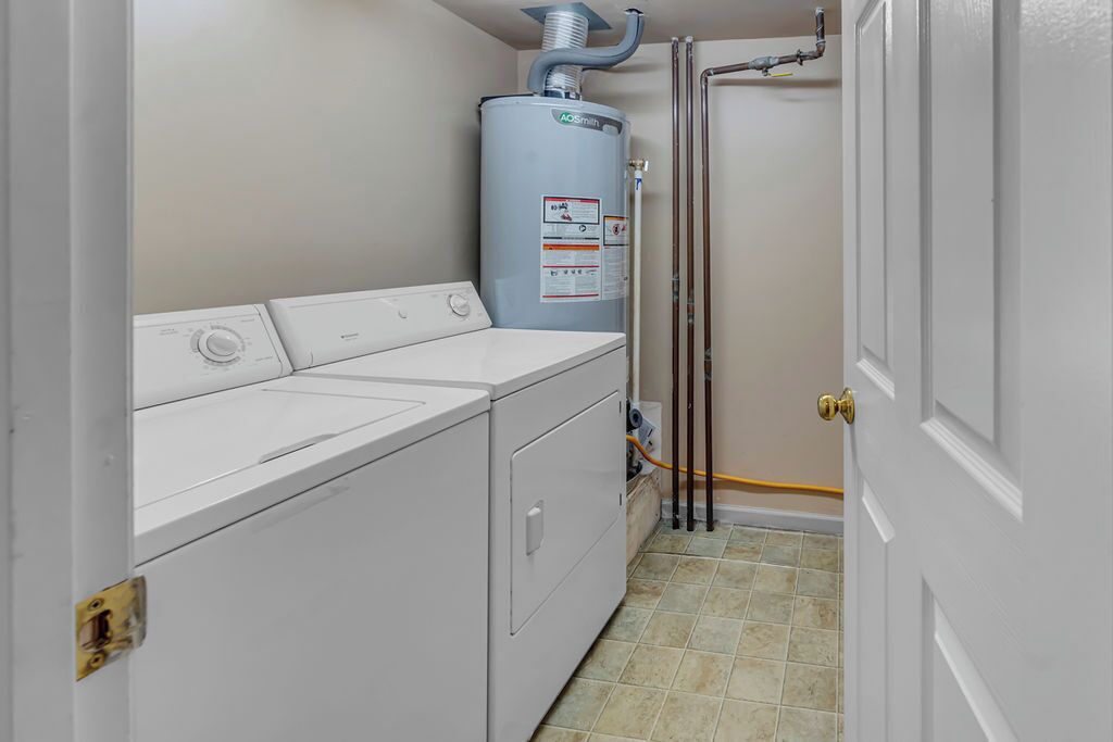 Een wasserette met een voorlader wasmachine en droger, een boiler, en een deur.