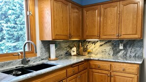 A kitchen with wooden cabinets, granite countertops, a stainless steel sink, and a window with a view of trees. - Quiet, relaxing home on Lake Watab in beautiful St. Joseph, MN near SJU and CSB (St Joseph)