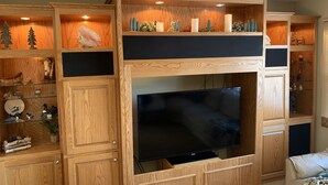 A wooden entertainment center with a flat-screen TV, shelves with decorative items, and a built-in seating area. - Quiet, relaxing home on Lake Watab in beautiful St. Joseph, MN near SJU and CSB (St Joseph)