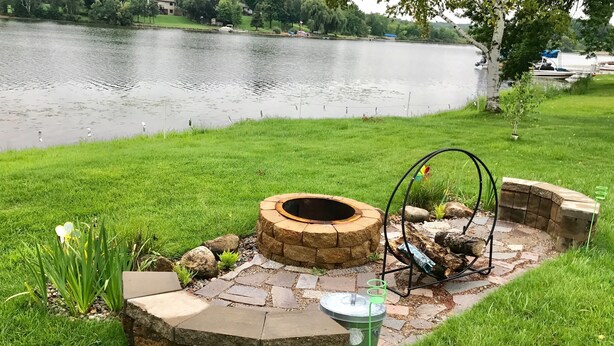 A stone fire pit with a metal frame and a green trash can nearby. - Quiet, relaxing home on Lake Watab in beautiful St. Joseph, MN near SJU and CSB (St Joseph)