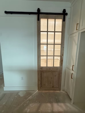 A room with a sliding door, a wooden door with a grid pattern, and a white wall with a single electrical outlet. - ON THE ROCKS 2.0 BIG LAKE 🎣 (Lake Charles)