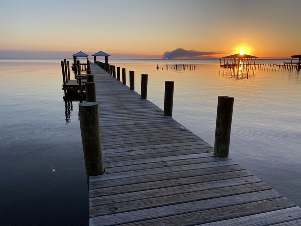 A wooden pier extending into calm waters with a sunset in the background.
