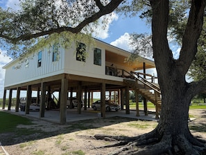 A two-story house with a wooden deck, a staircase, and a large tree in the foreground.