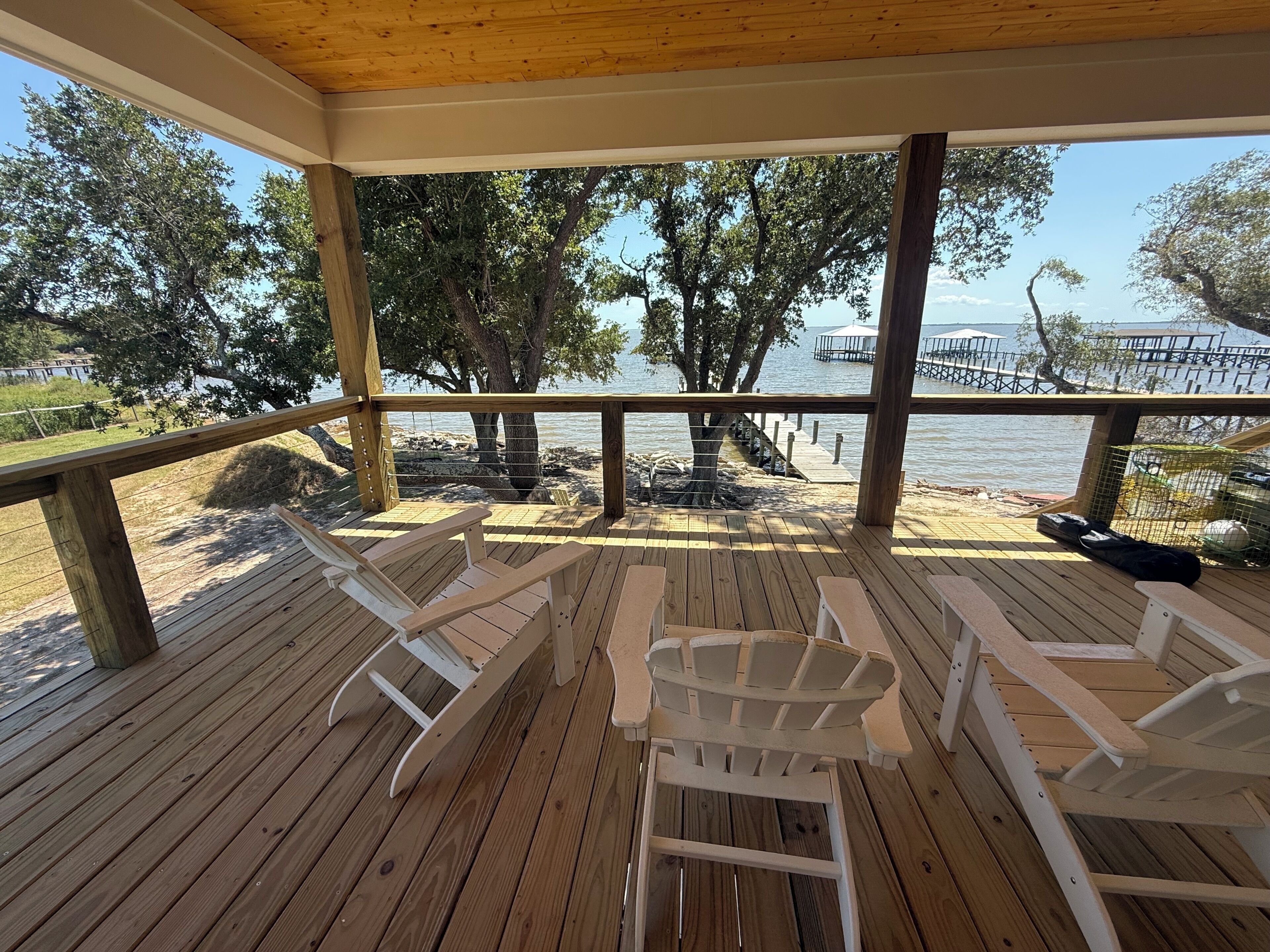 A wooden deck with white Adirondack chairs overlooking a lake, a dock, and trees.