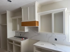 A kitchen with white cabinetry, a wooden shelf, and marble countertops.