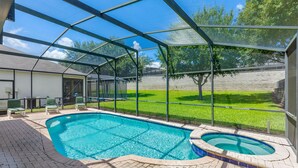 Une piscine extérieure couverte avec un jacuzzi, entourée d’un patio aménagé avec des chaises et un barbecue.