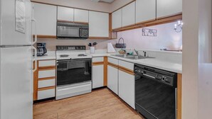 Una cucina moderna con mobili bianchi, microonde, piano cottura, forno e lavastoviglie.