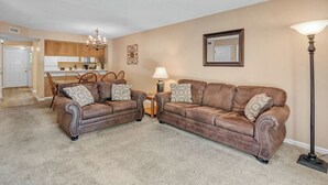 A living room with two brown leather sofas, a small table, a floor lamp, and a kitchen in the background. - two bedroom condo sleeps 8 persons (Gatlinburg)