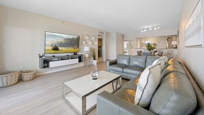 A modern living room with a flat-screen TV, a grey leather sofa, a white coffee table, and a minimalist design. - Luminous corner condo overlooking the bay | WIFI + Netflix + Parking (Sunny Isles Beach)