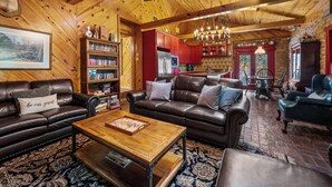 Un intérieur de chalet chaleureux avec des canapés en cuir, une table basse en bois, une bibliothèque et un coin repas agrémenté d’un lustre.