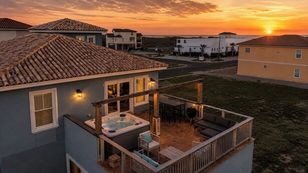 A residential building with a patio area featuring a hot tub, outdoor furniture, and a wooden deck.