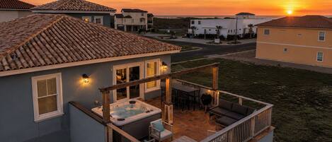 A residential building with a patio area featuring a hot tub, outdoor furniture, and a wooden deck.