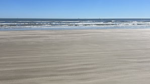 A wide sandy beach with gentle waves and a clear blue sky.