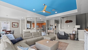A spacious living room with a ceiling fan, a sectional sofa, a coffee table, and a dining area in the background.