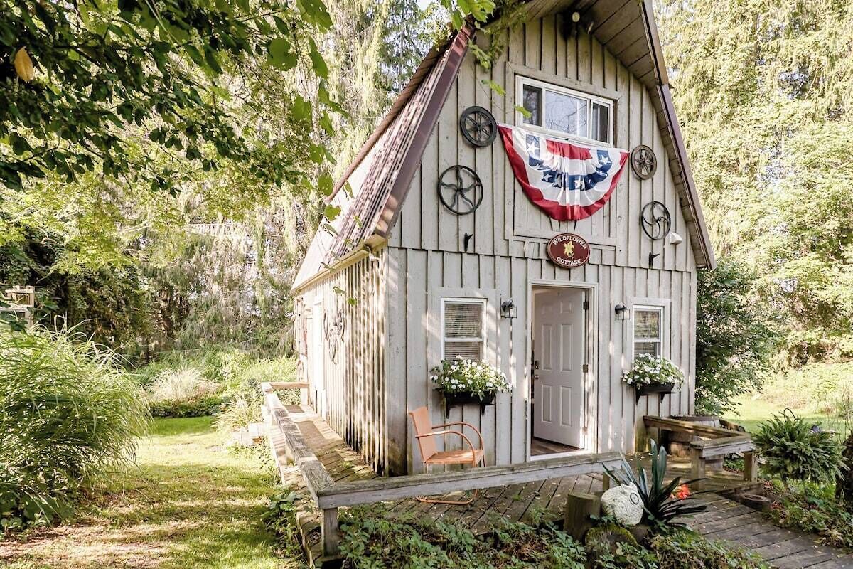 A wooden cabin with a porch, a flag, and a sign that reads 'Wildflower Cottage.'