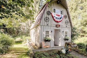 A wooden cabin with a porch, a flag, and a sign that reads 'Wildflower Cottage.'
