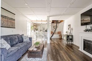 A spacious living room with a sofa, a fireplace, and a staircase leading to an upper level.