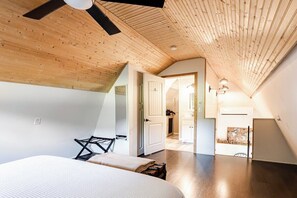 A bedroom with a sloped ceiling, a bed, a desk, and a view into the kitchen. - ⭐️Wildflower Country Cottage (Oxford)