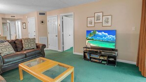 Ein Wohnzimmer mit einer Ledersofa, einem Glastisch, einem Flachbildfernseher und einem Bücherregal.
