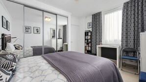 A modern bedroom with a large bed, a desk, a chair, and a wardrobe.