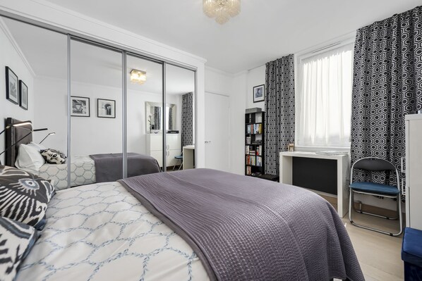 A modern bedroom with a large bed, a desk, a chair, and a wardrobe.