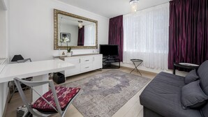 A modern living room with a white desk, a grey sofa, a large mirror, a flat-screen TV, and a patterned rug.