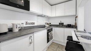 A modern kitchen with white cabinetry, a built-in oven, and a marble countertop.