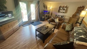 A living room with a brown leather sofa, a coffee table, a television on a wooden cabinet, and a sliding glass door leading to an outdoor area. - VACATION RENTAL- SLEEPS UP TO 10 -GOLDEN BC (Blaeberry)