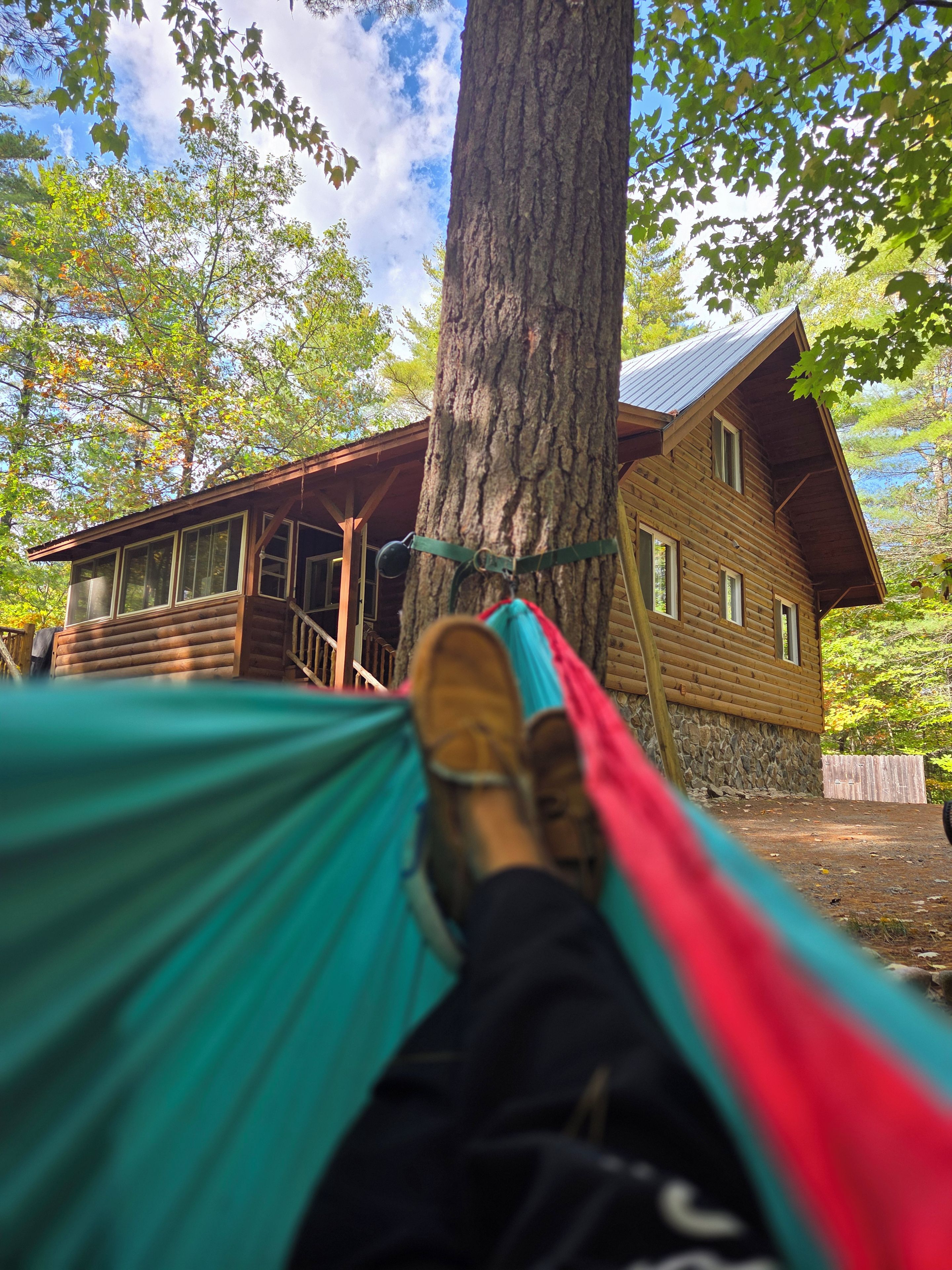 A hammock tied between two trees with a wooden cabin in the background.