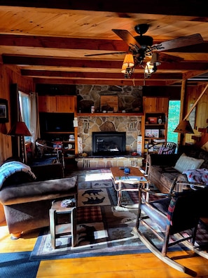 Een gezellig chalet interieur met een stenen open haard, houten meubels en een plafondventilator.