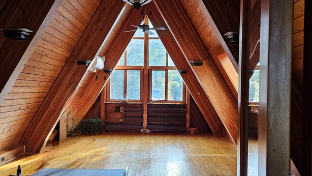 Une chambre mansardée avec des lambris en bois, un ventilateur de plafond et de grandes fenêtres.