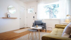 Ein Wohnzimmer mit einer Couch, einem runden Tisch, einem Sessel, einem Spiegel und einem Fenster mit Vorhängen.