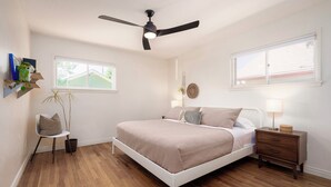 Ein Schlafzimmer mit Bett, Nachttisch, Sessel, Deckenventilator und Fenster.