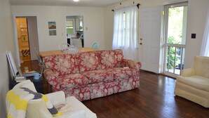 Una sala de estar con un sofá floral, un sillón blanco y una mesa de comedor de madera.