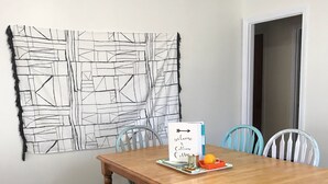 Un comedor con una mesa de madera, cuatro sillas, un banco y una obra de arte en la pared.
