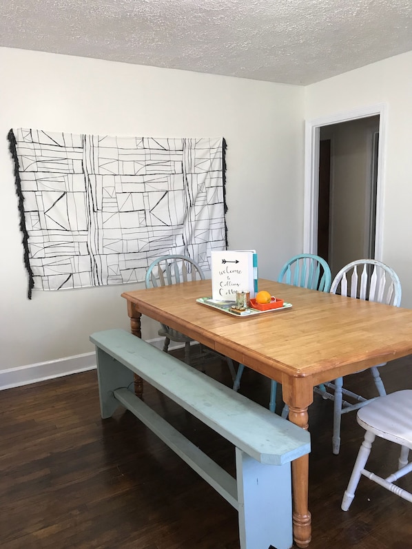 A dining area with a wooden table, four chairs, a bench, and a wall art piece.