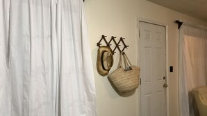 Una habitación con cortinas blancas, una puerta y un perchero de pared con un bolso tejido.