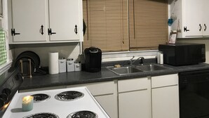 Una cocina con armarios blancos, estufa, fregadero y una ventana con persianas.
