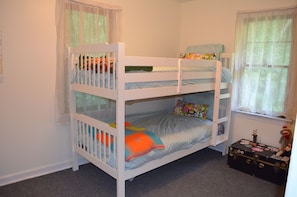 A bunk bed with a lower bunk, a window with sheer curtains, and a small table with a teddy bear.