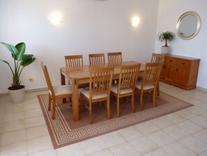 A dining area with a wooden table and chairs, a potted plant, a cabinet, and a patterned rug.