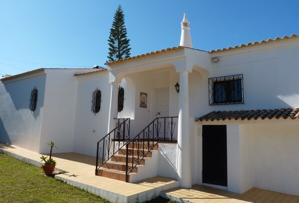 Un edificio de dos pisos con fachada blanca, techo de tejas y una escalera que conduce a la entrada.