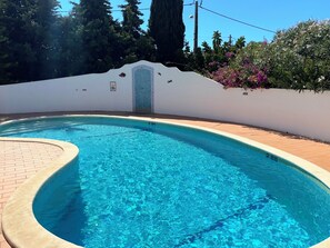 A swimming pool with a tiled edge, surrounded by a white wall with a decorative tile border and a small door.