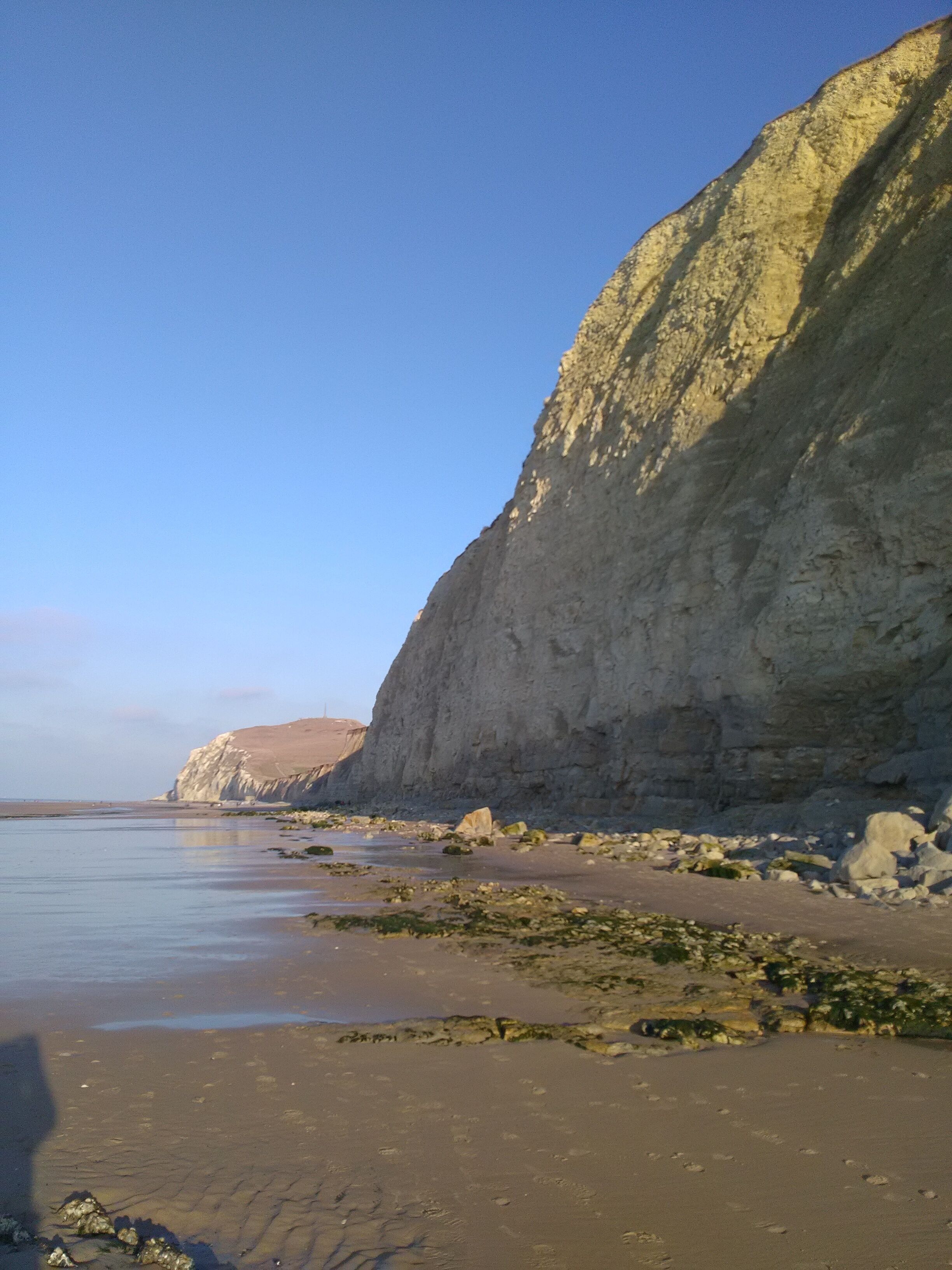 A coastal landscape with a sandy beach, rocky outcrops, and cliffs.