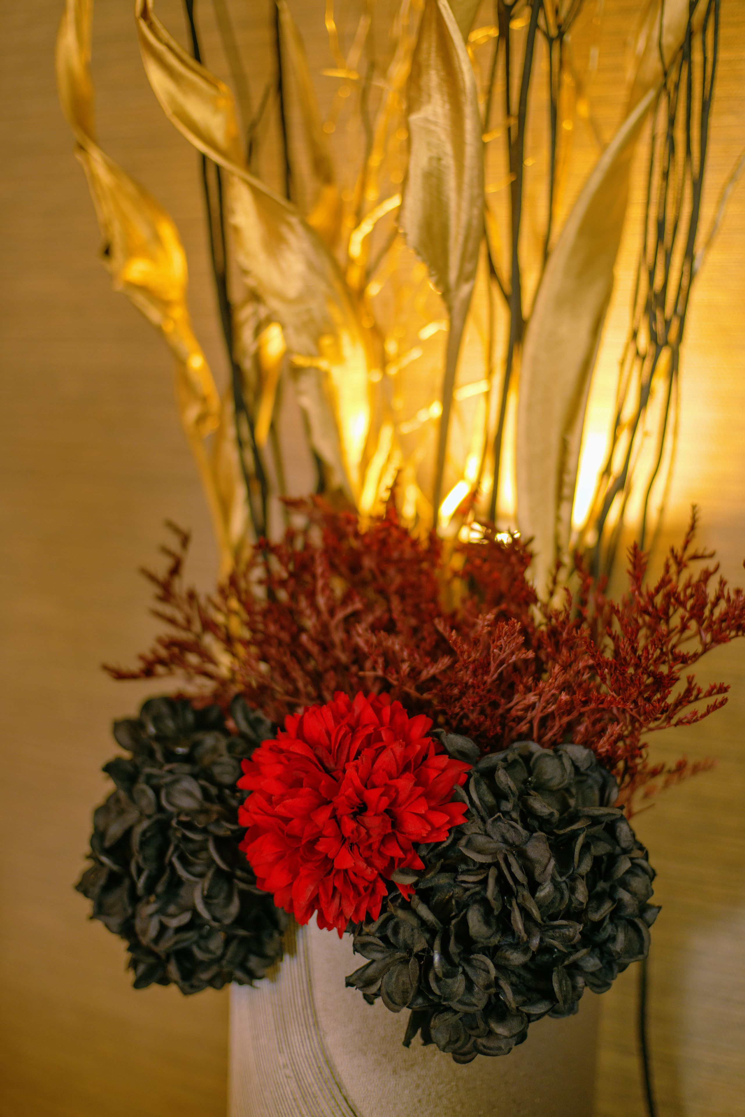 A vase with red and black flowers and dried foliage.
