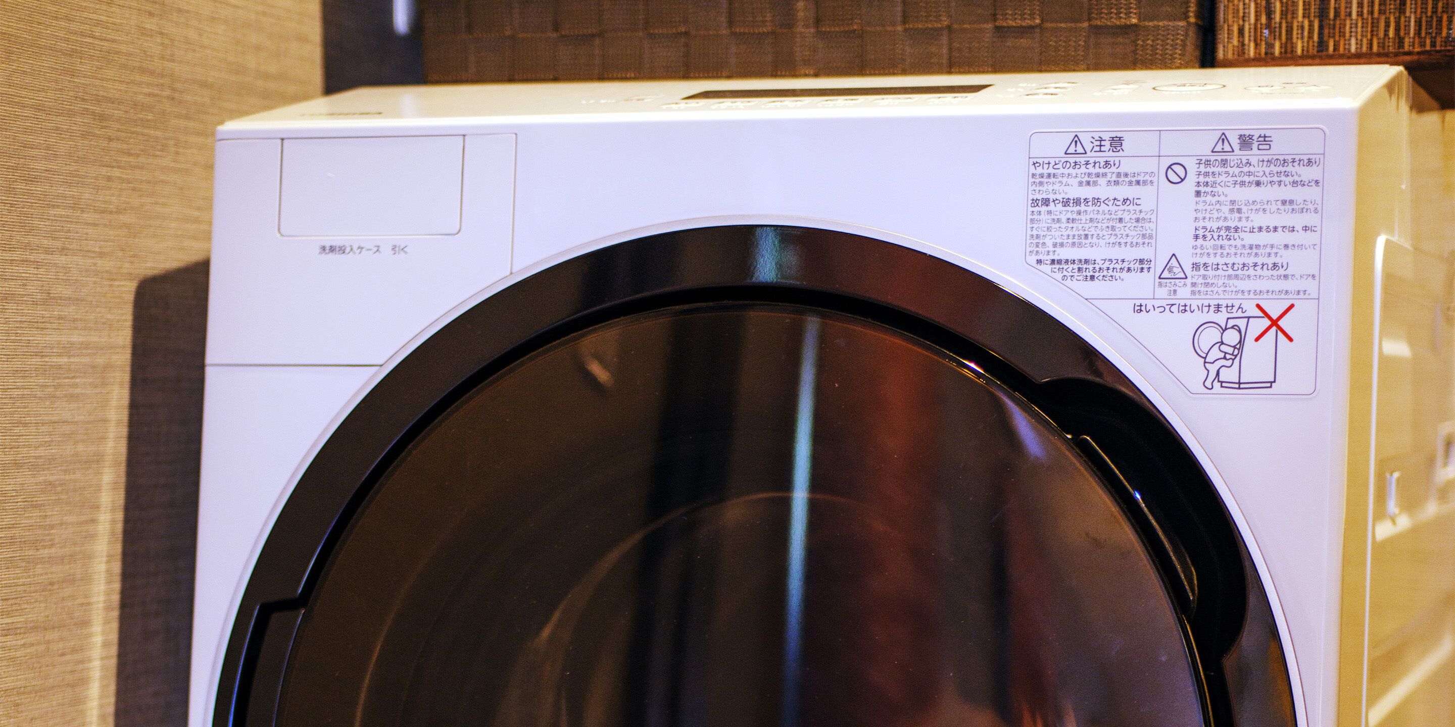 A front view of a white washing machine with a closed door, a control panel, and safety instructions on the right side.