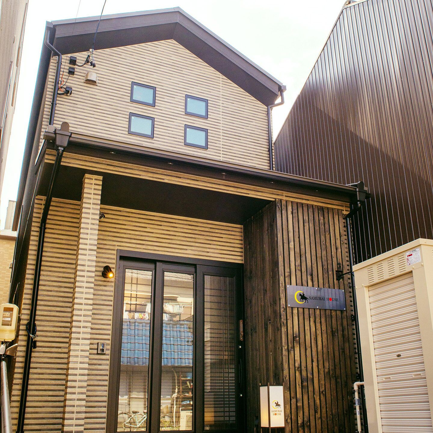 Un edificio con fachada de madera, una puerta de cristal grande y un letrero que dice 'Samurai House'.