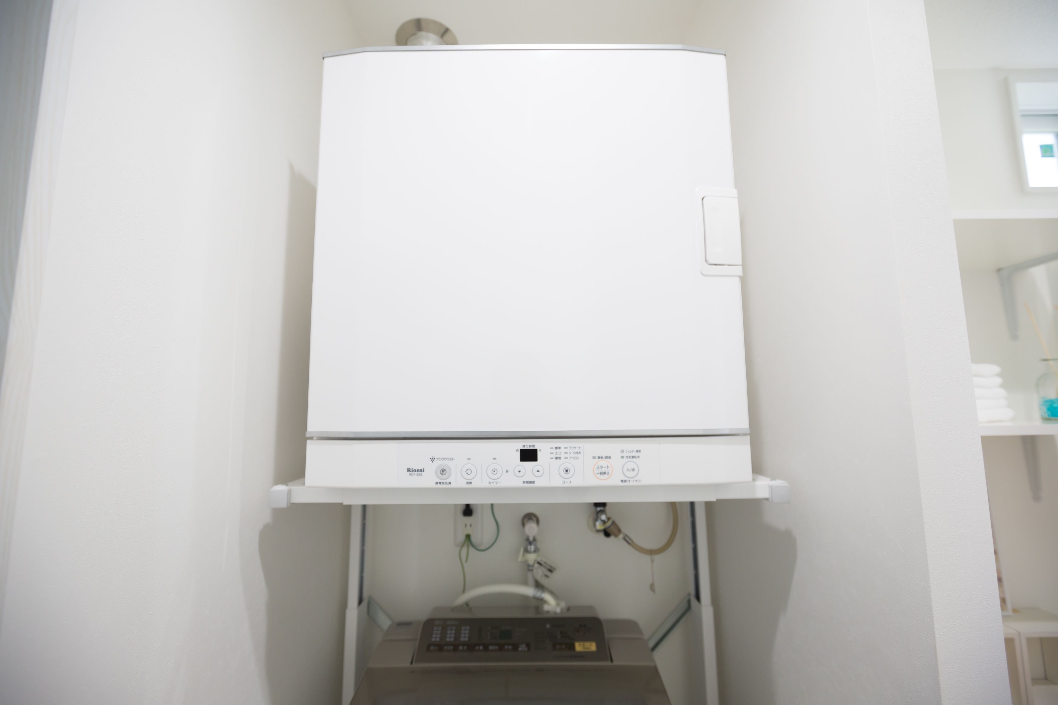 Un calentador blanco y moderno fijado a la pared, con panel de control y conexiones de fontanería visibles.