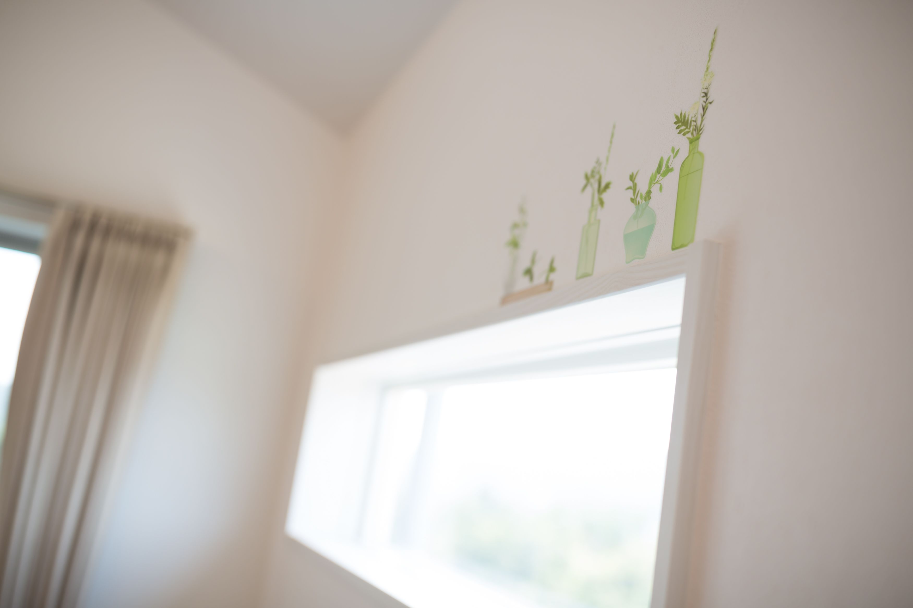 A room with a window, a curtain, and wall decorations of plants.