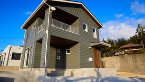 A two-story house with a balcony, a satellite dish, and a concrete wall in the background. - The Pool Resort Villa ICHIGOICHIE (Onna)