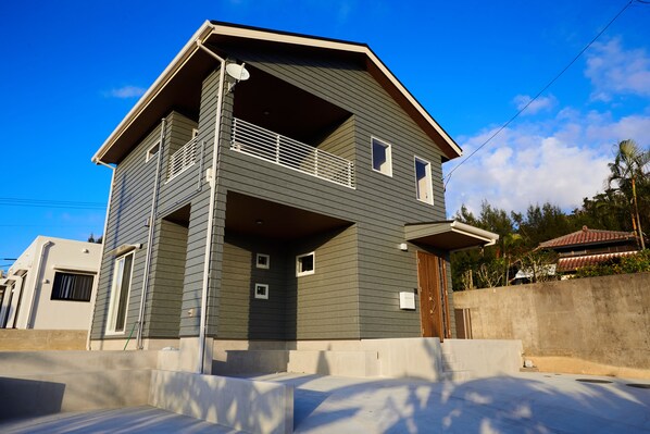A two-story house with a balcony, a satellite dish, and a concrete wall in the background. - The Pool Resort Villa ICHIGOICHIE (Onna)